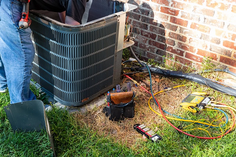 3 Tips to Prevent AC Breakdown During a Heat Wave. Photo of a black air conditioning unit installed outside of a brick home.