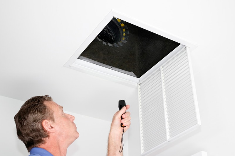 Man looking into an air duct with a flashlight.